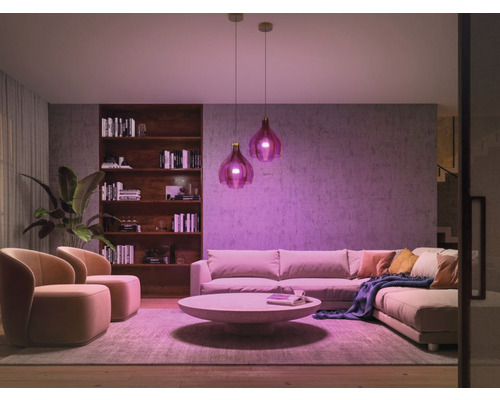 Ljust vardagsrum med soffa, fåtöljer, soffbord, bokhylla och två hänglampor för en mysig atmosfär.