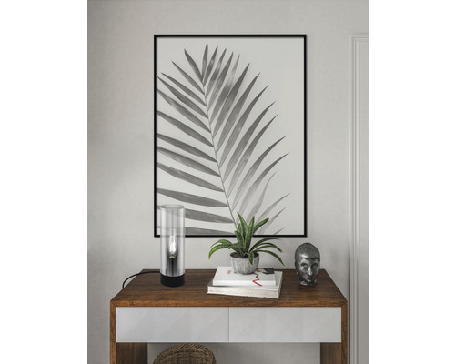 Dekorativ scen med bord, lampa, växt och inramad palmbladsbild