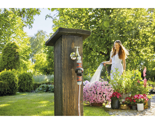 Kvinna vattnar blommor med en trädgårdsslang vid en kran i trädgården