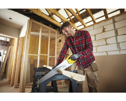 Hantverkare sågar trä på en arbetsbänk i ett renoverat rum.