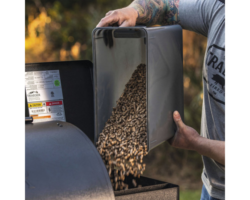 En person fyller pellets i en grill.