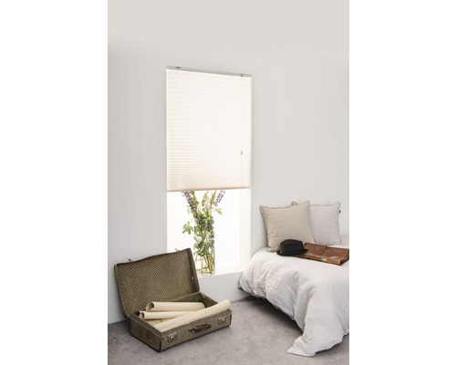 Ljust rum med plisségardin vid fönstret, säng och öppen resväska