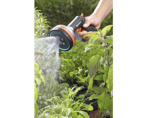 En hand håller ett Gardena duschhuvud och vattnar växter.