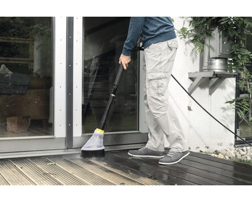 En person rengör en träterrass med en borste och en vattenslang.