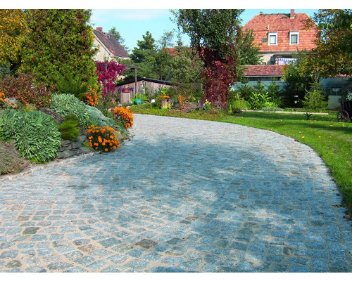 Stenlagd väg med natursten i en trädgård med blommor och träd.