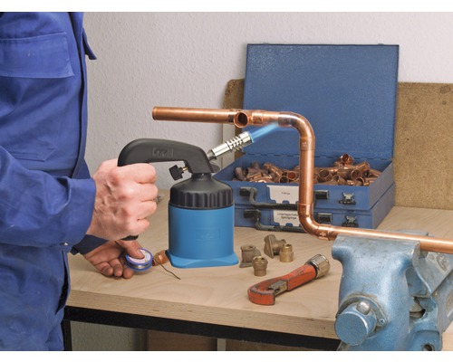 Man löder kopparrör med en lödbrännare, kopplingar och verktyg på en arbetsbänk