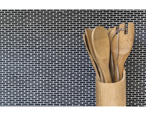 Träskedar och spatlar i en bambubehållare framför en mosaikvägg