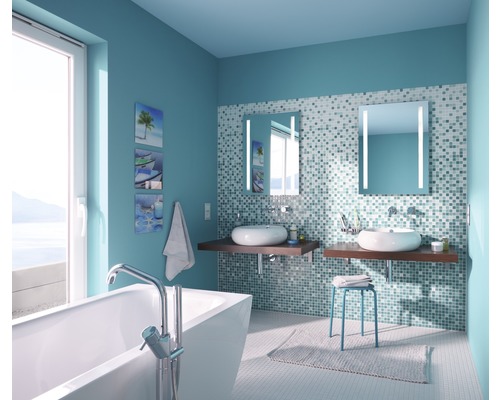 Ljust badrum med badkar, två handfat, belysta speglar och mosaikplattor på väggarna