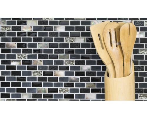 Köksredskap av trä i en behållare framför en mosaikvägg