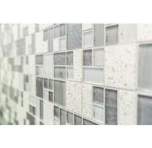 Närbild av en vägg med mosaikplattor i olika gråtoner och texturer.