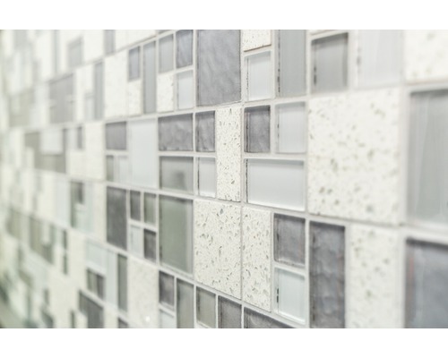 Närbild av en vägg med mosaikplattor i olika gråtoner och texturer.