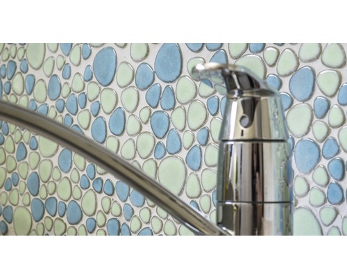 Närbild av en vattenkran framför en vägg med mosaikplattor i stenmönster