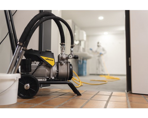 Färgspruta i bruk med person i skyddskläder i bakgrunden