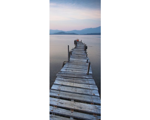 Träbrygga leder till vatten med berglandskap i bakgrunden