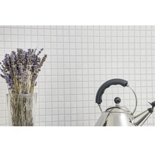 Bunt lavendel i ett glas och en vattenkokare i rostfritt stål mot en bakgrund av vita plattor.