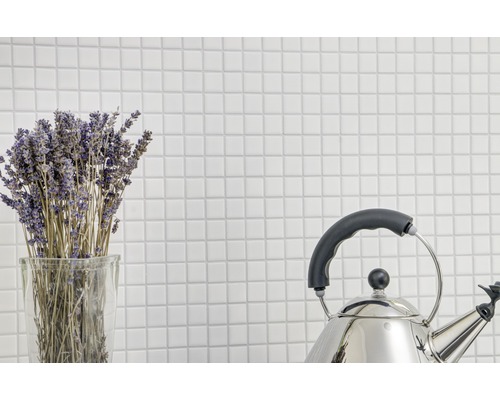 Bunt lavendel i ett glas och en vattenkokare i rostfritt stål mot en bakgrund av vita plattor.