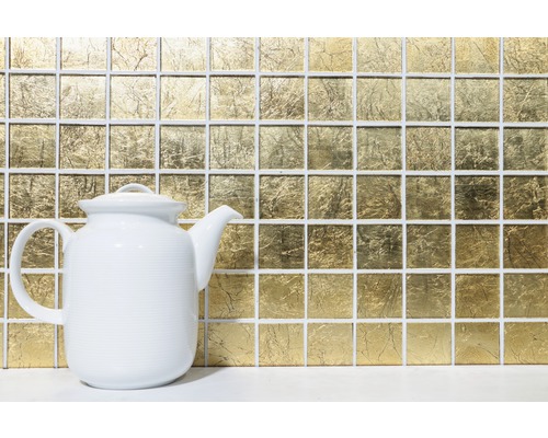 Guldfärgad mosaik i bakgrunden med en vit tekanna i förgrunden