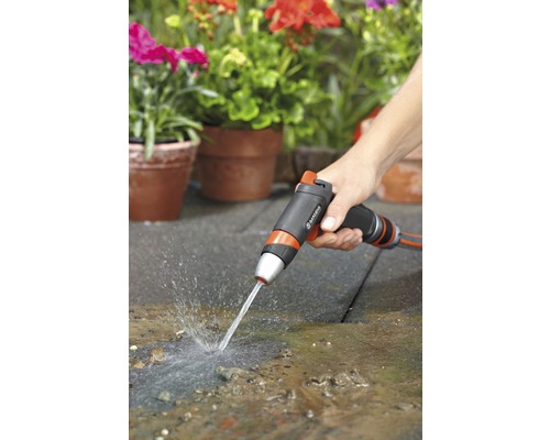En person använder en trädgårdsspruta för att rengöra en terrass framför planterade krukor.