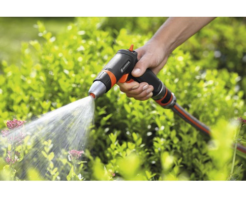 En hand håller i en Gardena trädgårdsspruta som sprutar vatten på växter.