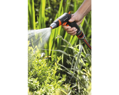 En hand håller i en trädgårdsspruta som sprutar vatten på växter.