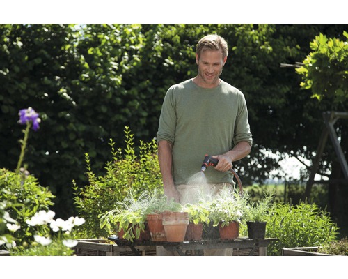 En man vattnar växter i krukor med en trädgårdsslang i trädgården.