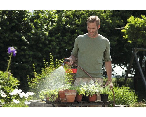 En man vattnar växter i trädgården med en trädgårdsspruta och en trädgårdsslang.