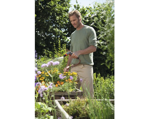 Man vattnar blommor med trädgårdsslang i trädgården.