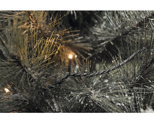 Detaljbild av en julgran med dekorativ snö och en ljusslinga