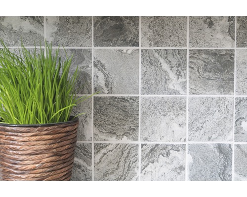 Fyrkantiga väggplattor med marmormönster bredvid en kruka med gräs