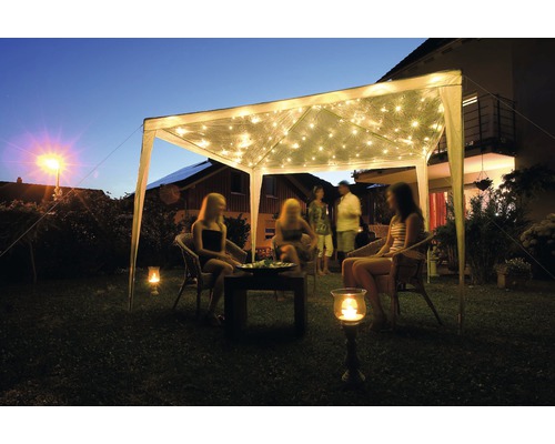 Trädgårdsscen med paviljong, ljusslingor och sittande personer