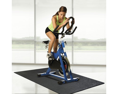 Kvinna tränar på en blå spinningcykel på en svart matta