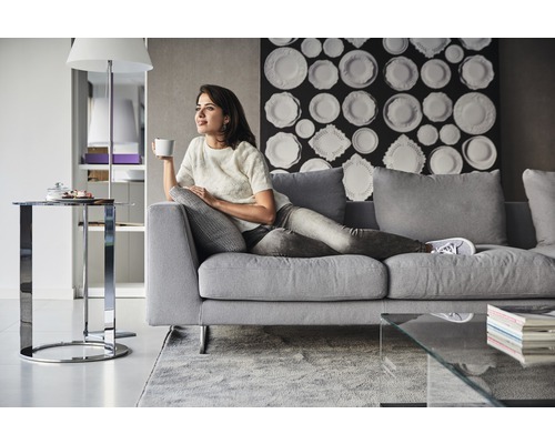 Kvinna kopplar av på en grå soffa i ett vardagsrum med modern inredning.