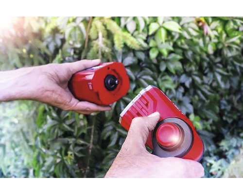 Två händer håller en elektronisk mårdskrämma framför grönt lövverk