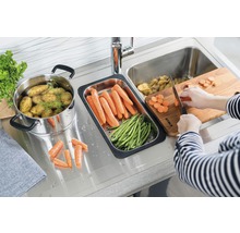 Köksscen med diskho, skärbräda, grönsaker och kastrull med potatis