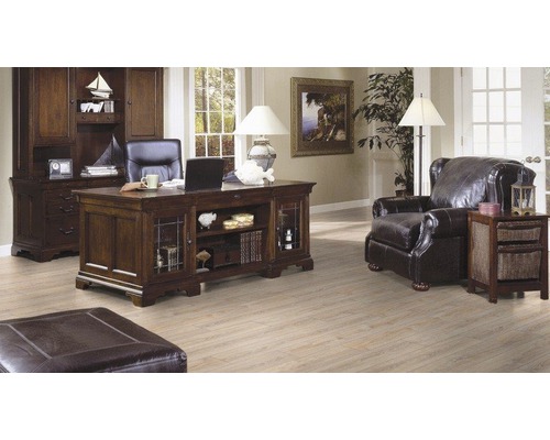 Kontor med skrivbord, bokhylla, fåtölj och ottoman i ett ljust rum.