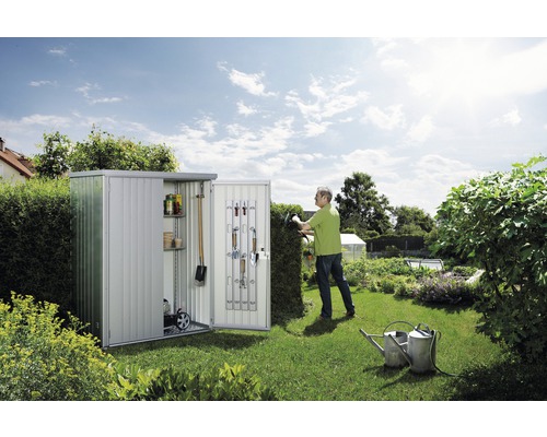 Trädgårdsscen med metallredskapsbod, trädgårdsredskap och trädgårdsmästare som klipper en häck