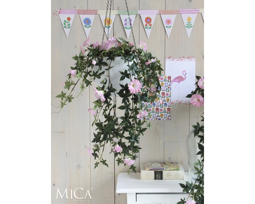 Dekorativ hängväxt med rosa blommor i vit kruka framför trävägg