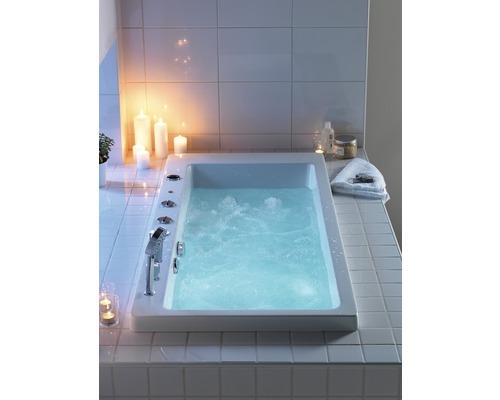 Inbyggt badkar med vatten, armatur och kontrollelement i ett ljust badrum med ljus