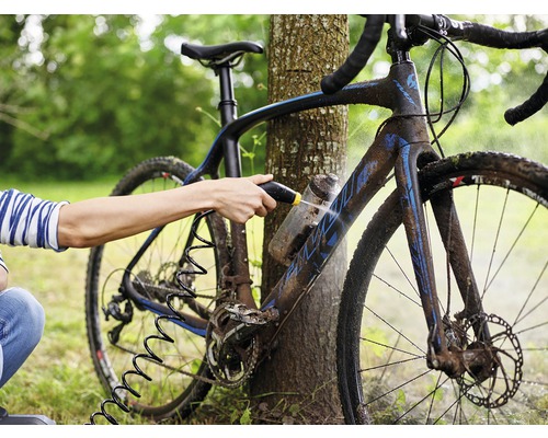 En person rengör en cykel med en högtryckstvätt utomhus.