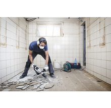 Man med skyddsglasögon och hörselskydd slår bort kakel från ett golv med en borrhammare