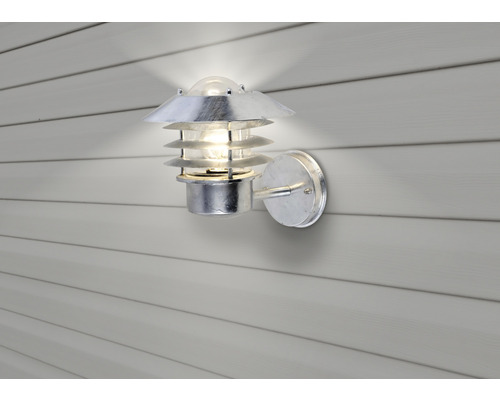 En silverfärgad utomhusvägglampa med en flerskiktad lampskärm är fäst på en vägg.