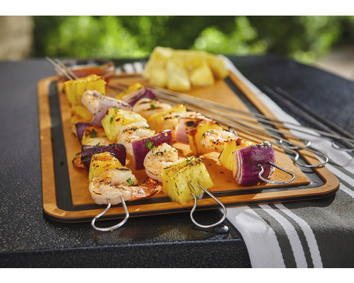Grillspett med ananas, räkor och rödlök på en träbräda.