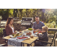 Familjen njuter av en grillfest utomhus med en gasgrill i bakgrunden.