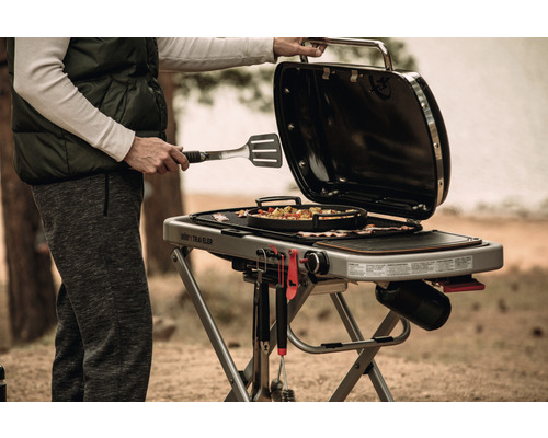 Person använder Weber Traveler gasolgrill utomhus med grillverktyg och mat
