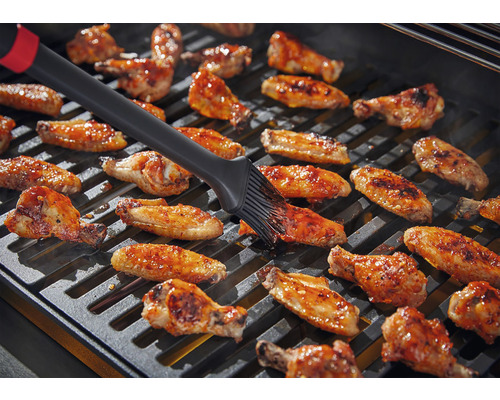 Kycklingvingar borstas på en grill.