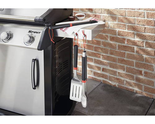 Gasolgrill med grillverktyg och handduk mot en tegelvägg