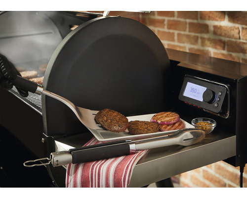 Detaljvy av en grill med hamburgare, lök, grilltång och kryddor