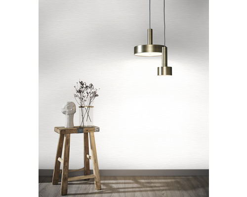 Scen med en hänglampa, en vas med blommor, en skulptur på en pall framför en tapet.