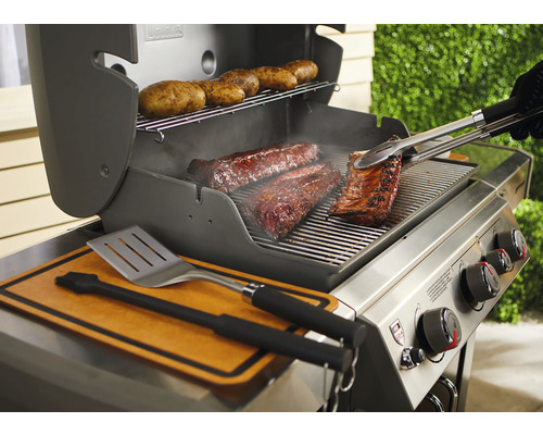 Grill med revbensspjäll, kött och potatis på gallret, grilltång och stekspade redo.