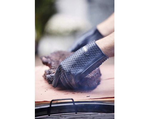 En person med grillhandskar som rör kött på papper.